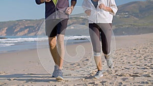 Elderly couple in sportswear running on sandy beach together