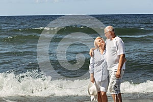 An elderly couple stand hugging on the beach by the sea, look at each other, communicate