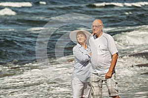 An elderly couple is standing on the beach by the sea