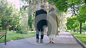 An elderly couple strolling peacefully in the park. A man and woman enjoying a leisurely walk amidst nature.