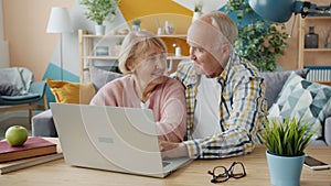 Elderly couple using computer at home talking typing enjoying internet content
