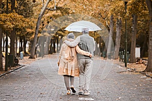 Elderly, couple walk in park with umbrella and fresh air, outdoor in nature in fall for exercise and retirement together