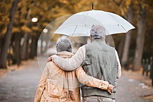 Elderly, couple walk in park with umbrella and fresh air, outdoor in nature in fall for exercise and retirement together