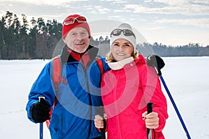 Elderly couple walking with nordic walking poles in snowy winter park