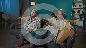 An elderly couple is watching something on TV movie or program. The woman is unhappy asking to switch. The man is