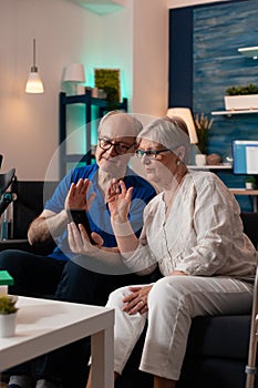 Elderly couple waving at video call webcam using smartphone