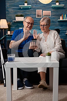 Elderly couple waving at video call webcam using smartphone
