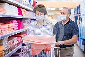 Elderly couple wearing protective masks choosing bedding in supermarket