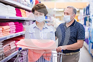 Elderly couple wearing protective masks choosing bedding in supermarket