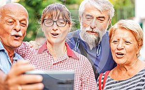 Elderly couples taking selfie with smartphone - Old friends reunion having fun outdoors with each other