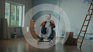 An elderly disabled man in a wheelchair. The pensioner looks around and plans repairs. Room with window, ladder