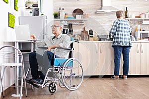 Elderly disabled person working on laptop in kitchen