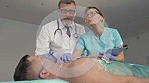 An elderly doctor and nurse examining a critically ill male patient in the emergency room.