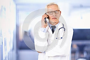 Elderly doctor talking with his patient on his mobile phone while standing in hospital