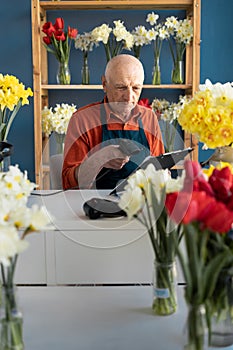 An elderly European male flower seller reads a barcode to arrange delivery.