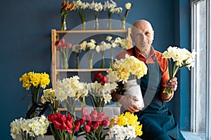 An elderly European man sitting on table holds bright bouqeuts.