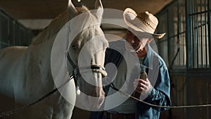 Elderly farmer cleaning horse in stable