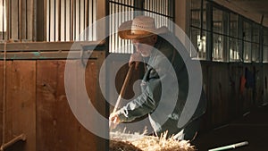 Elderly farmer throwing straw into stall