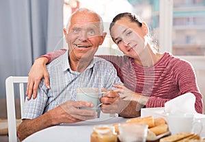 Elderly father and adult daughter talk and drink tea in the kitchen