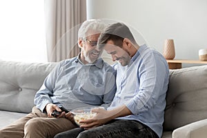 Elderly father grownup son laughing eating popcorn enjoy weekends together