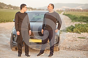 Elderly father and young son standing next to car in nature on road trip.