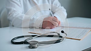 Elderly female doctor is carefully writing on a medical record.