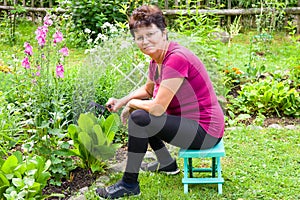 Elderly female gardener is loosening a soil with a rake in a beautiful flower garden in summer