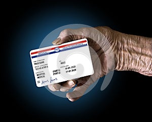 An elderly female hand holds a mock United State government Medicare Health Insurance card. It is a generic card