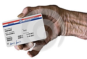 An elderly female hand holds a mock United State government Medicare Health Insurance card. It is a generic card