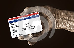 An elderly female hand holds a mock United State government Medicare Health Insurance card. It is a generic card.