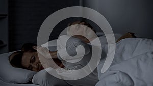 Elderly female pressing hands against ears cant sleep, man snoring in bed