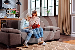 Elderly female sitting on sofa with her young-adult daughter