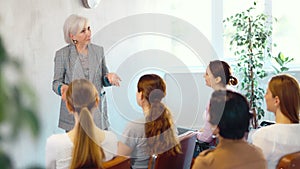 Elderly female teacher giving lecture to group of students in classroom