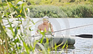 Elderly fisherman fishing off a dinghy near reeds