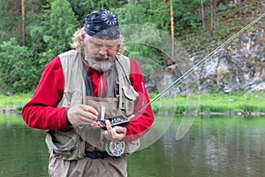 An elderly fisherman with a fishing or spinning rod and with a fishing box for tackle