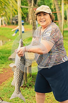 Elderly fisherwoman holding a Pintado fish, looking forward and