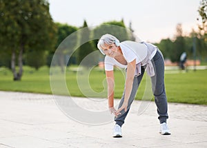 Elderly fit woman in wireless headphones doing stretching exercises before jogging outside photo