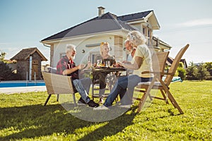 Elderly friends having an outdoor lunch in the backyard by the swimming pool
