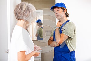 Elderly frustrated housewife shows plumber malfunction in bathroom