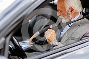 Elderly gentleman buckling up in his luxury car before a drive