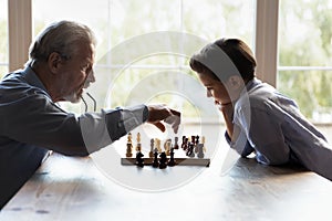 Elderly granddad teaching little boy grandkid to play chess game