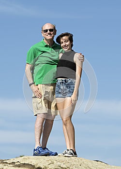 Elderly grandfather and teenage granddaughter standing on a rock