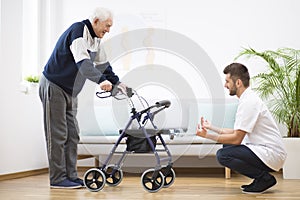 Elderly grandfather with walker trying to walk again and helpful male nurse supporting him