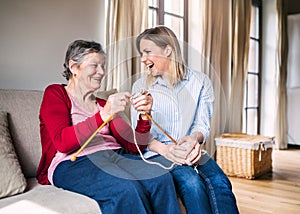 Elderly grandmother and adult granddaughter at home, knitting.