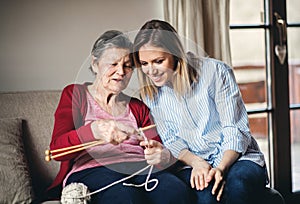 Elderly grandmother and adult granddaughter at home, knitting.