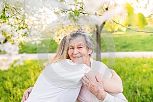 Elderly grandmother and granddaughter hugging in spring nature.