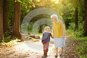 Elderly grandmother and her little grandchild walking together in sunny summer park. Friendship of grandma and grandson