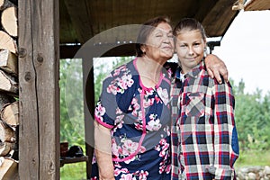 Elderly grandmother kisses twelve old granddaughter, portrait on veranda of wooden summer house