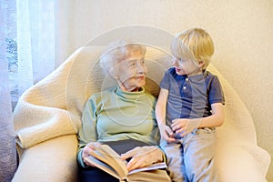 Elderly grandmother and little grandchild reading a book at home. Grandma and grandson