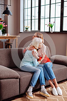 Elderly granny having a hug with attractive granddaughter on sofa